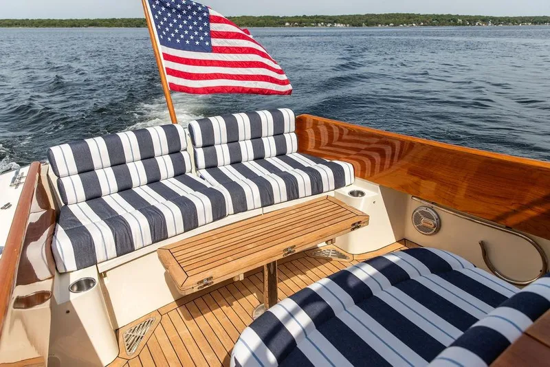 Slide: The Image of 2005 Hinckley Picnic Boat EP with striped seating and American flag on open water. - 5