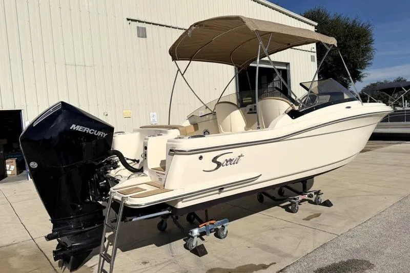 Slide: The Image of 2023 Scout 215 Dorado boat with Mercury engine, parked outdoors under a canopy. - 2