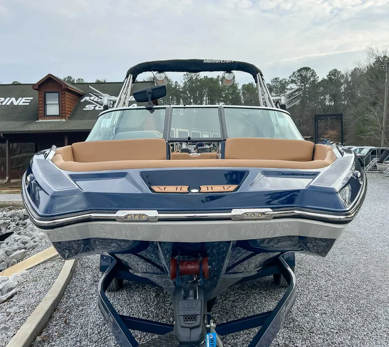 Slide: The Image of 2021 MasterCraft XT22 boat, blue, on gravel path in front of log cabin. - 4
