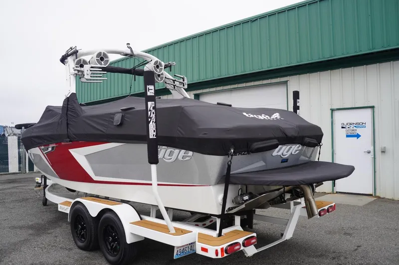 Slide: The Image of 2022 Tigé 22RZX boat on trailer, covered, parked near green building. - 2