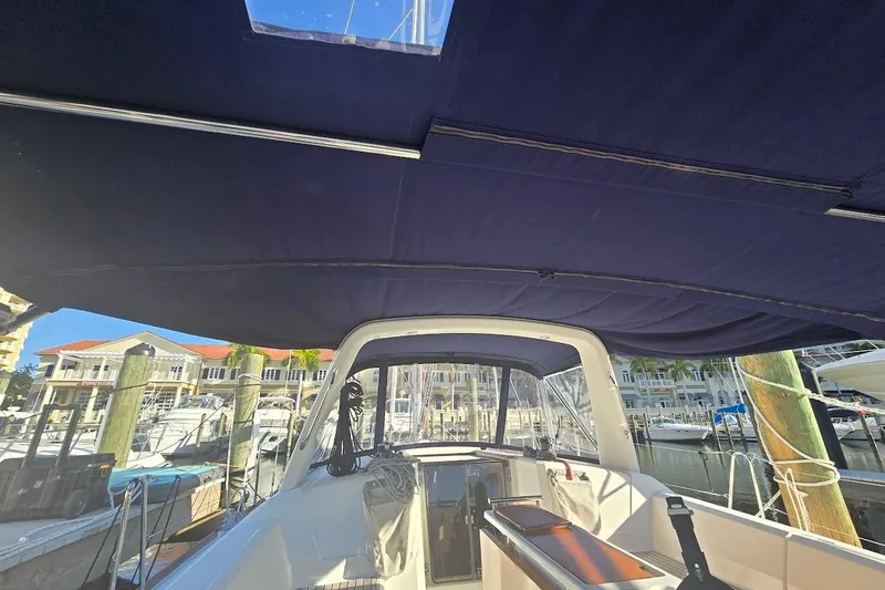 Slide: The Image of 2023 Beneteau Oceanis 38.1 cockpit view with marina backdrop, featuring blue canopy. - 28