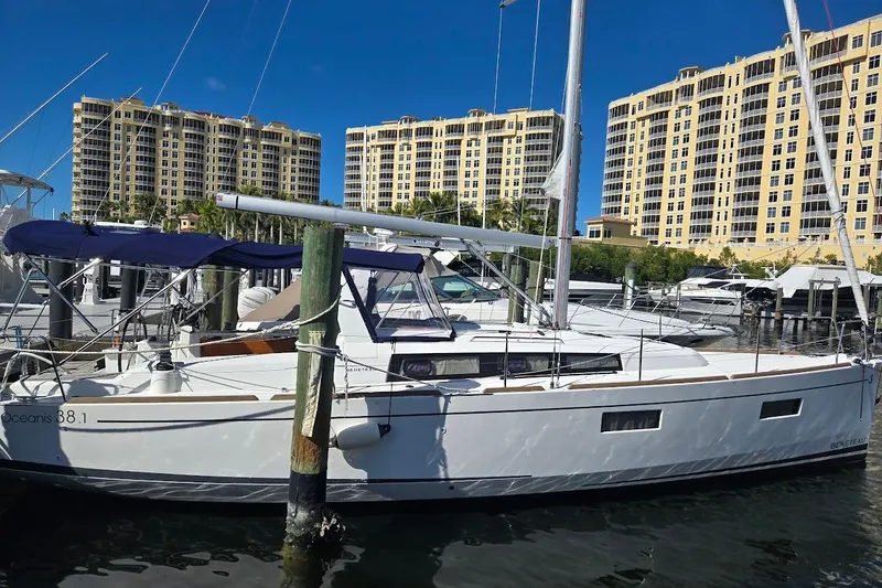 Slide: The Image of 2023 Beneteau Oceanis 38.1 sailboat docked at marina with tall buildings in background. - 90