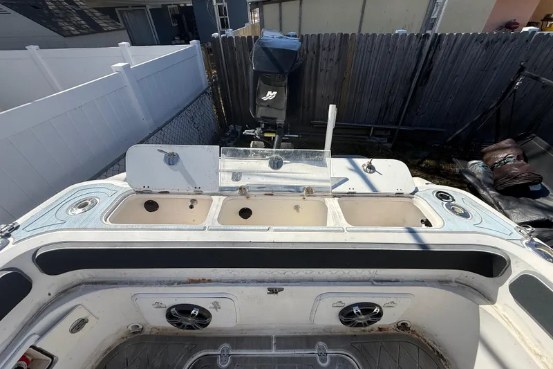 Slide: The Image of 2003 Glasstream 273 SCX boat interior with storage compartments and motor in a fenced yard. - 59