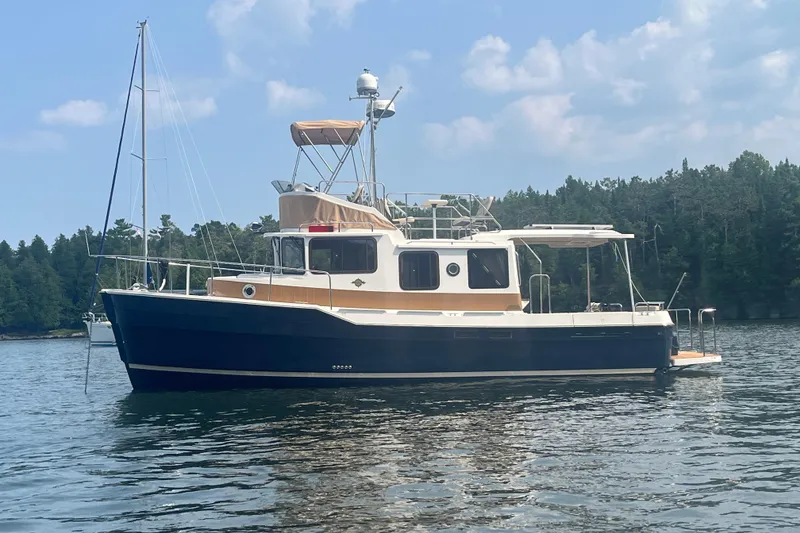 The Image of 2023 Ranger Tugs R-31 CB boat on calm water, surrounded by trees and blue sky. - 0