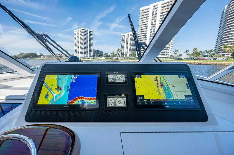 Slide: The Image of 2023 Viking 48 Sport Tower helm with navigation screens, cityscape in background. - 21