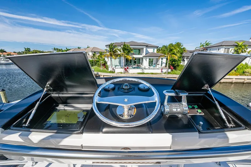 Slide: The Image of 2023 Viking 48 Sport Tower helm with navigation screens and controls, docked near waterfront homes. - 45