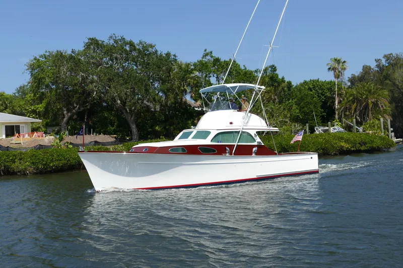 Slide: The Image of 1949 Rybovich Sport Fish boat navigating a scenic, tree-lined waterway. - 5