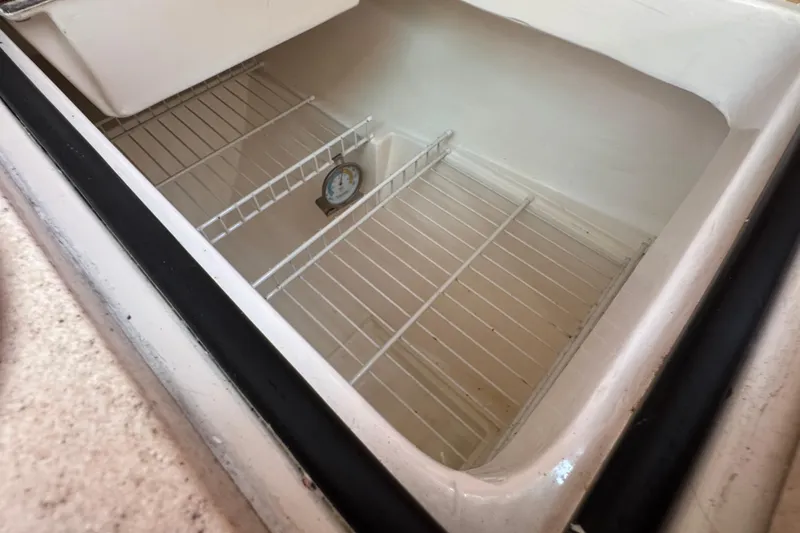 Slide: The Image of Empty refrigerator compartment in a 1997 Catalina 36 MkII boat, featuring wire shelves and a thermometer. - 30