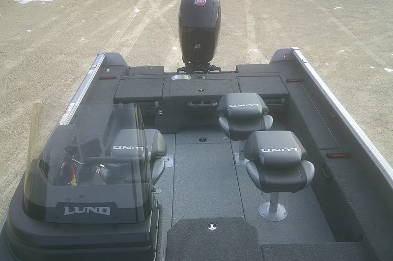 Slide: The Image of 2026 Lund 1875 Impact XS SS boat interior with seating and motor, on sandy ground. - 8