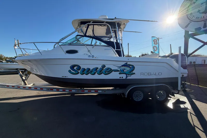 Slide: The Image of 2017 Robalo R265 Walkaround boat on trailer, featuring "Susie" graphic, under clear blue sky. - 11
