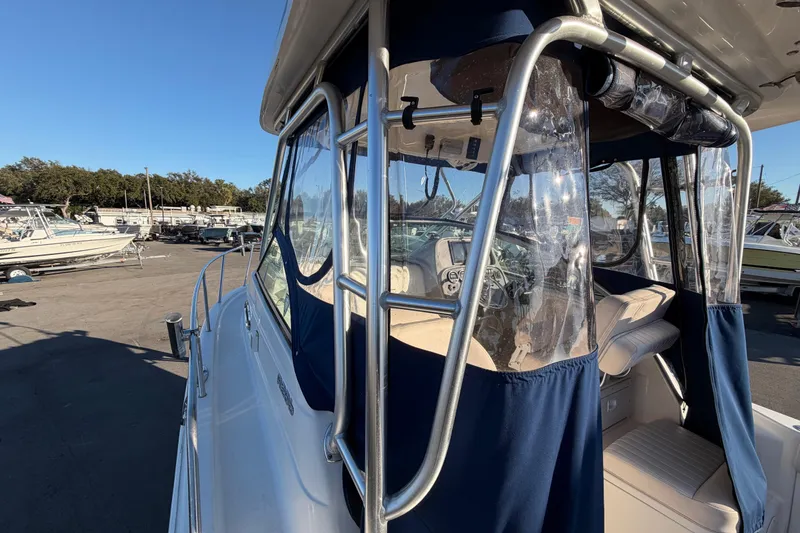 Slide: The Image of 2017 Robalo R265 Walkaround boat with blue canopy and clear panels in a marina setting. - 49