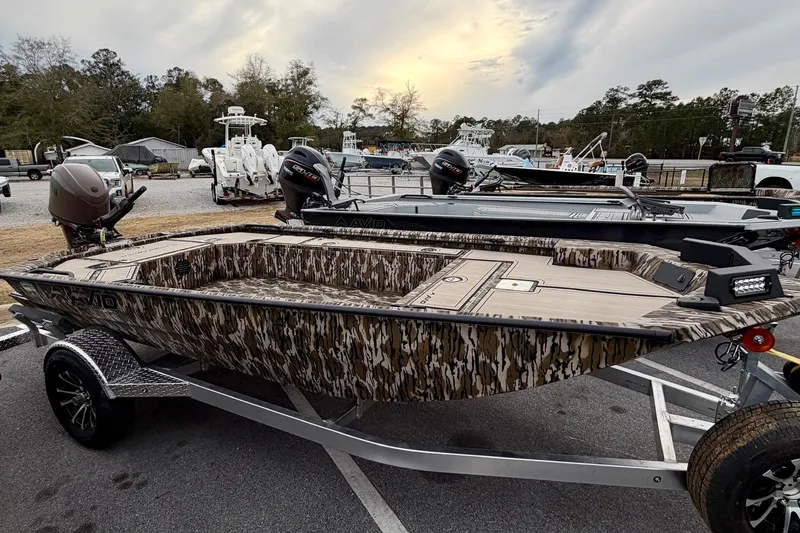 The Image of 2026 Avid 16 Commander boat with camouflage design on a trailer in a parking lot. - 0