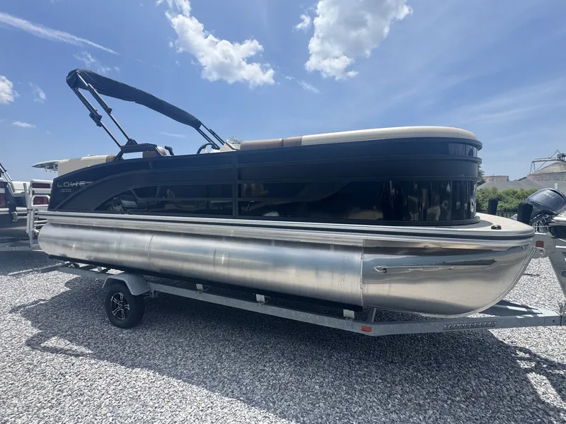 The Image of A 2026 Lowe LS Walk Thru 210 pontoon boat on a trailer in a gravel lot. - 1