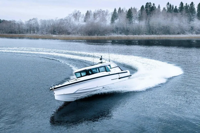 Slide: The Image of 2026 Axopar 38 Cross Cabin boat on a serene, icy lake with snowy forest backdrop. - 2