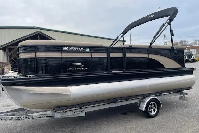 The Image of 2022 Bennington 20 SLX pontoon boat on trailer, black and beige design, parked outdoors. - 1