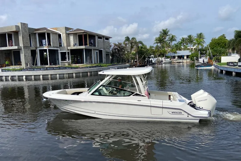 Slide: The Image of 2021 Boston Whaler 280 Vantage cruising in a scenic canal with modern homes. - 6