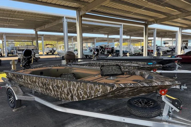 The Image of 2026 Avid 18 Commander boat with camouflage design on a trailer in a covered storage area. - 0