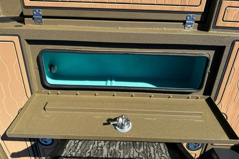 Slide: The Image of Open storage compartment in 2026 Avid 18 Commander boat, featuring teal interior and secure latch. - 18