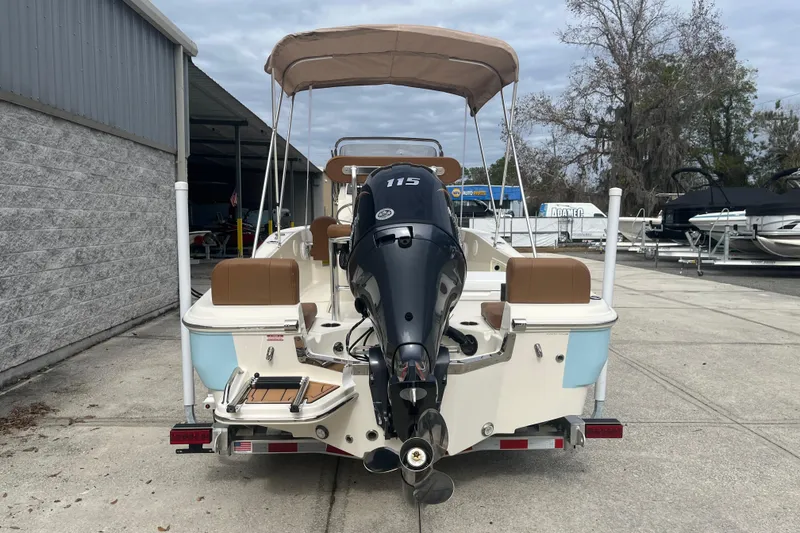 Slide: The Image of 2026 Pioneer 180 Sportfish boat with outboard motor and canopy, parked outdoors. - 3