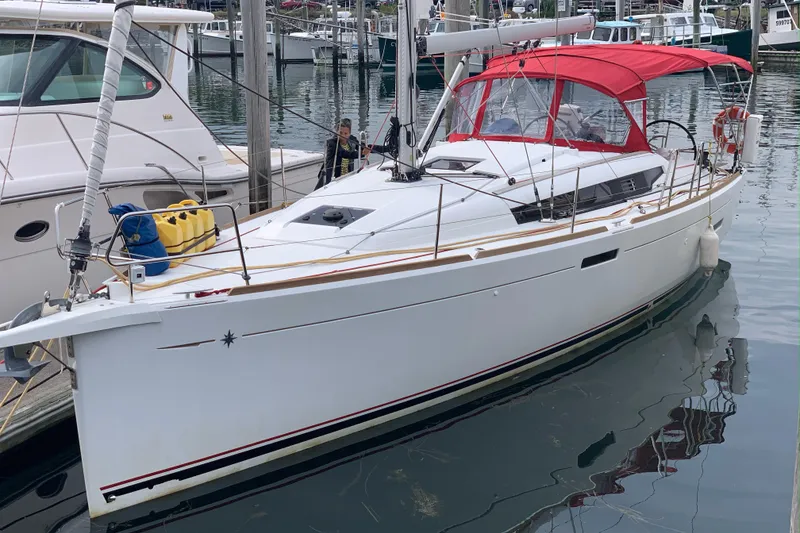 Slide: The Image of 2017 Jeanneau Sun Odyssey 389 sailboat on land, with red canopy, near houses and greenery. - 2
