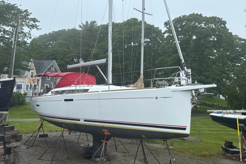 Slide: The Image of 2017 Jeanneau Sun Odyssey 389 sailboat on stands, surrounded by greenery and houses. - 6