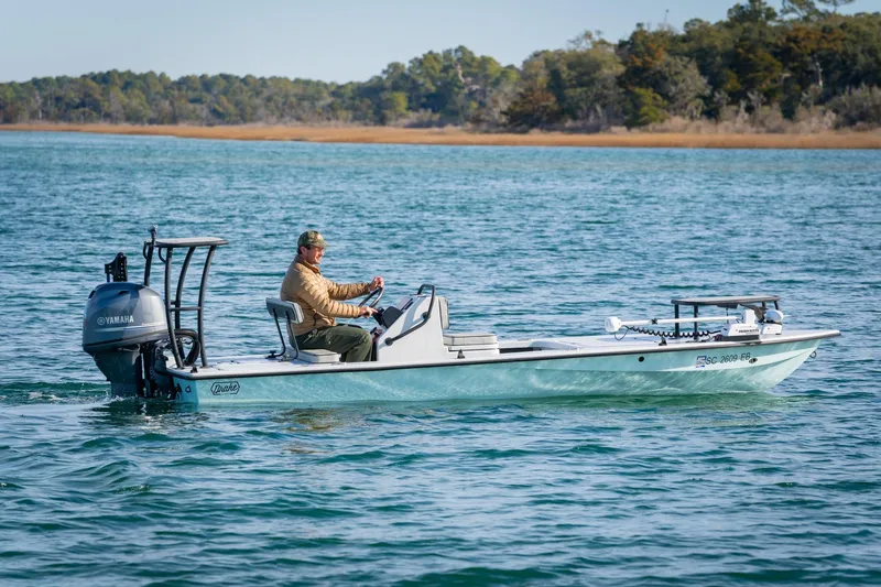 Slide: The Image of 2021 Drake Nomad boat on water with Yamaha engine, man steering, scenic background. - 1
