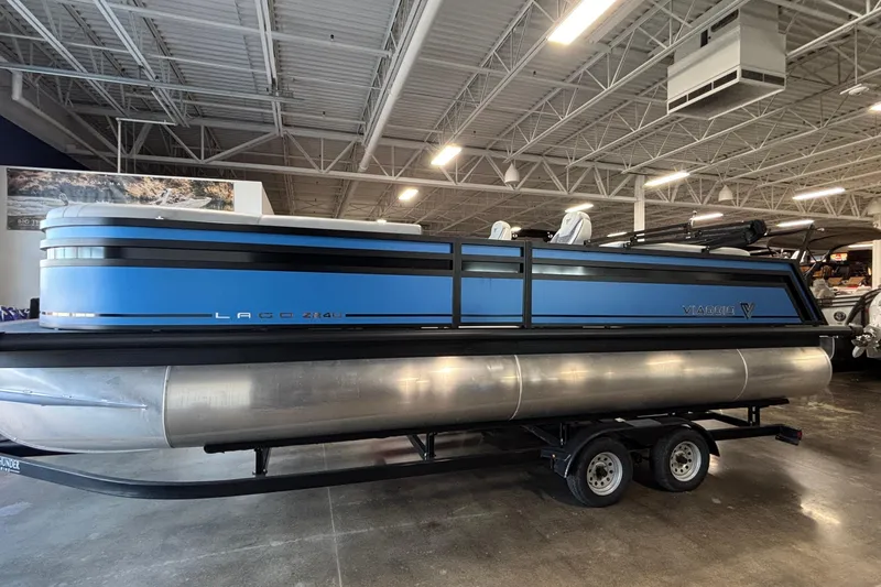 The Image of 2026 Viaggio Z24U pontoon boat in showroom, featuring sleek blue design and dual-axle trailer. - 0
