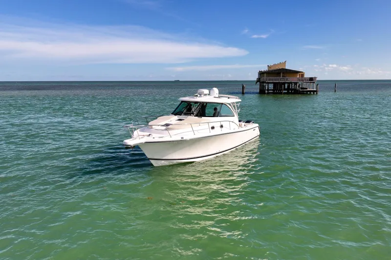 Slide: The Image of 2016 Pursuit OS 385 Offshore boat on turquoise water near a stilt house. - 12
