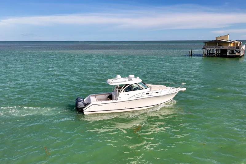 Slide: The Image of 2016 Pursuit OS 385 Offshore boat cruising on turquoise waters near a coastal building. - 14