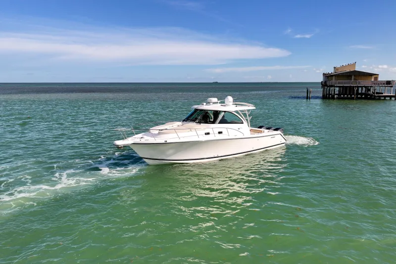 Slide: The Image of 2016 Pursuit OS 385 Offshore boat cruising on turquoise waters near a coastal building. - 19
