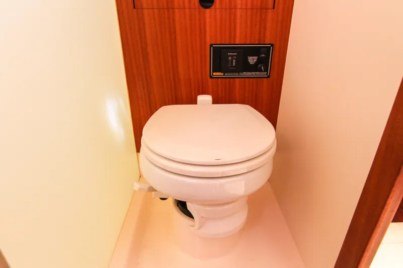 Slide: The Image of 2016 Pursuit OS 385 Offshore boat bathroom with a white toilet and wooden paneling. - 58