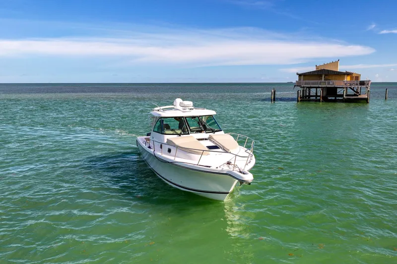 Slide: The Image of 2016 Pursuit OS 385 Offshore boat on turquoise water near a stilt house. - 9