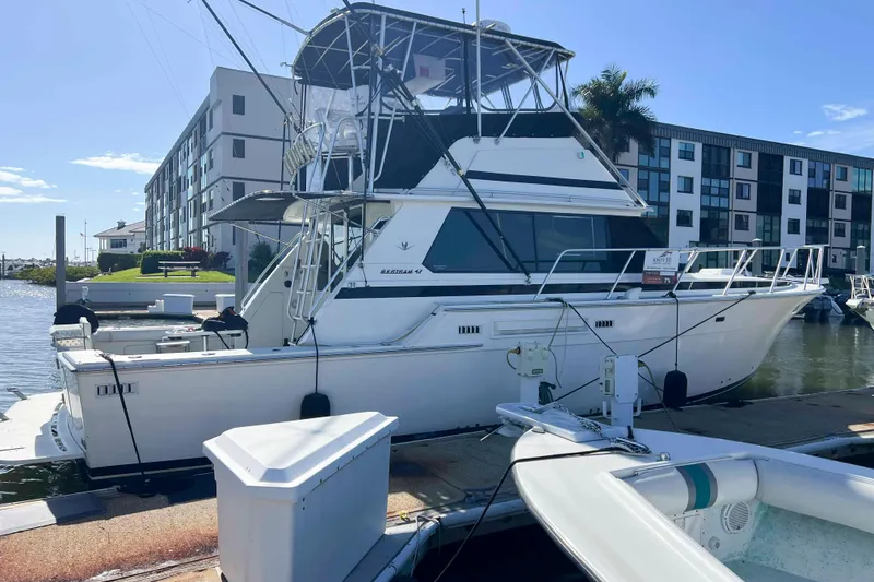 Slide: The Image of 1986 Bertram 42 Convertible yacht docked at marina, with modern buildings in background. - 2
