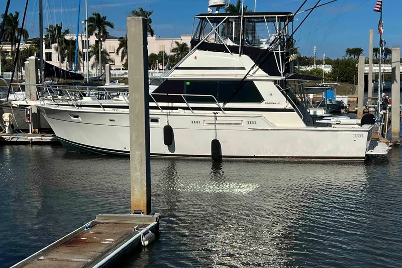 Slide: The Image of 1986 Bertram 42 Convertible yacht docked at marina, surrounded by calm water and palm trees. - 4