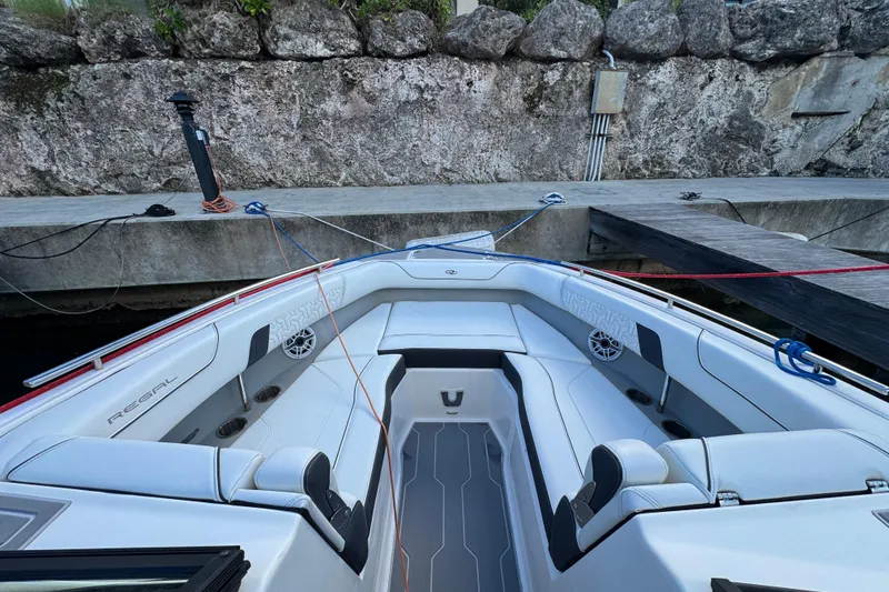 Slide: The Image of 2024 Regal LX9 boat interior with white seating, docked by a stone wall. - 5
