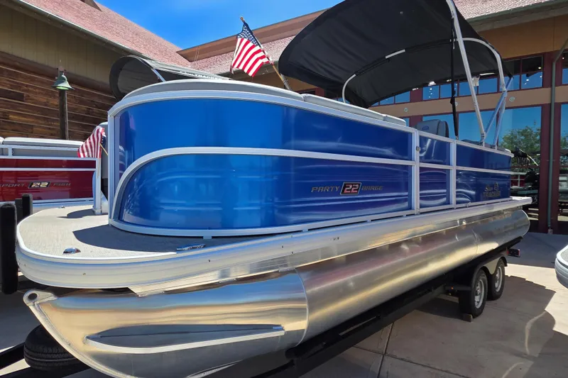 The Image of 2026 Sun Tracker Party Barge 22 DLX pontoon boat with American flags, parked outdoors. - 0