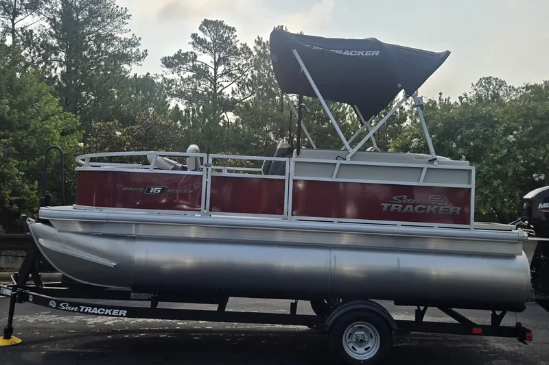 The Image of 2026 Sun Tracker Bass Buggy 16 XL Select pontoon boat on trailer, surrounded by trees. - 0