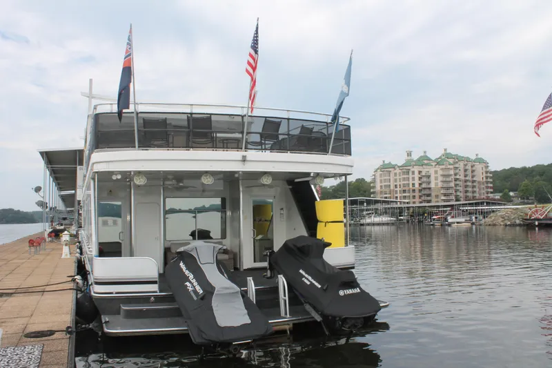 Slide: The Image of 2008 Sharpe 105 Custom Houseboat docked with jet skis, flags, and waterfront view. - 15