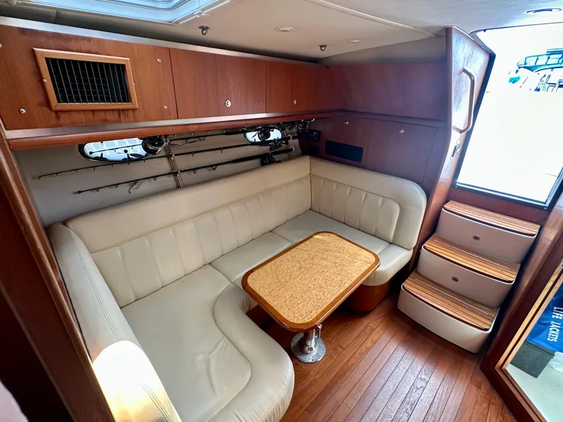 Slide: The Image of 2005 Tiara Yachts 3600 Open interior with beige seating, wooden table, and fishing rods. - 25