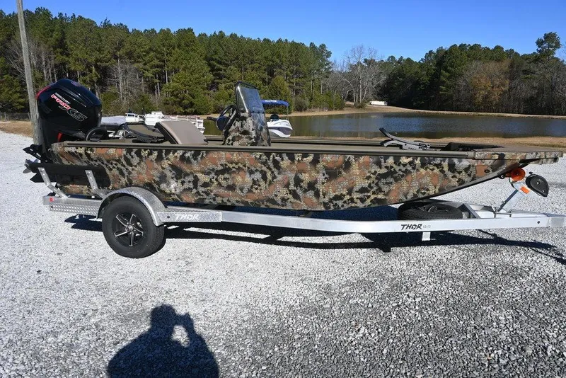 The Image of 2026 Thor 1900 Lake Hammer Center Console Elite boat on trailer, camo design, outdoor setting. - 1