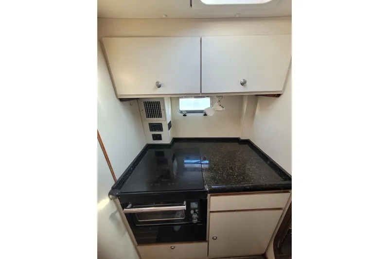 Slide: The Image of Compact kitchen area in a 1995 Lagoon TPI boat with black countertop and white cabinets. - 8