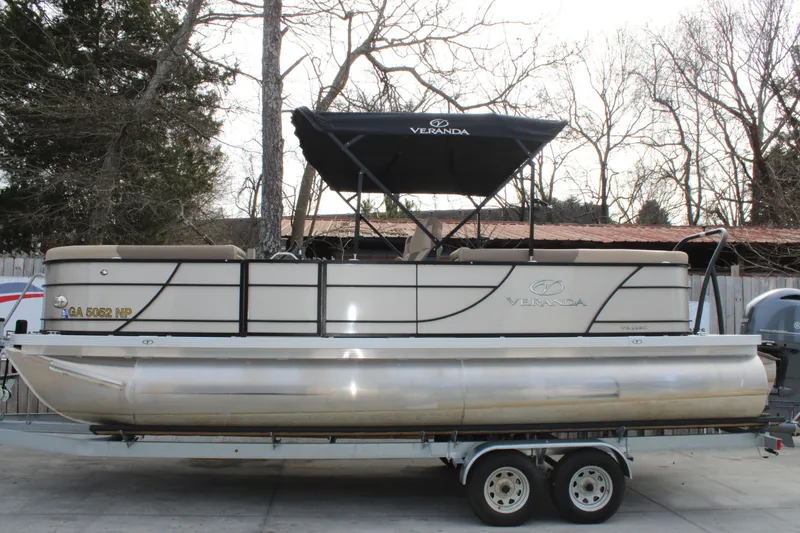 Slide: The Image of 2023 Veranda VR22RC pontoon boat on trailer, parked outdoors with trees in background. - 2