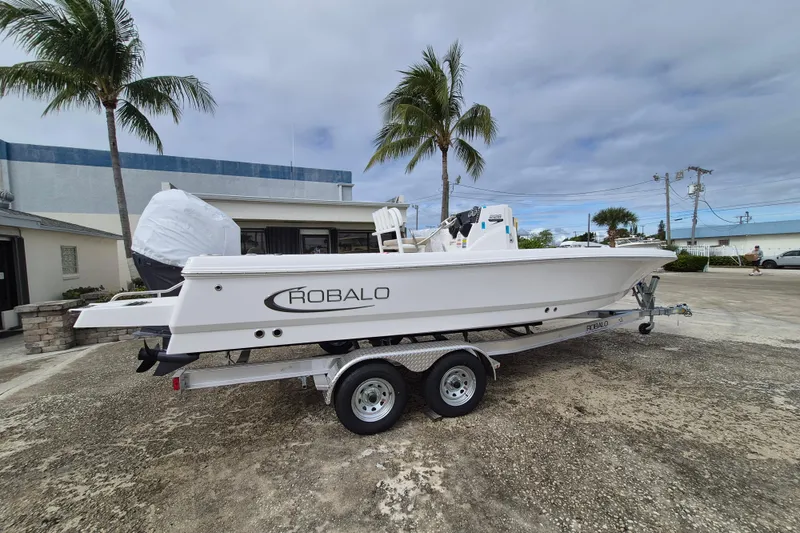 Slide: The Image of 2026 Robalo 226 Cayman boat on trailer, parked outdoors with palm trees. - 2