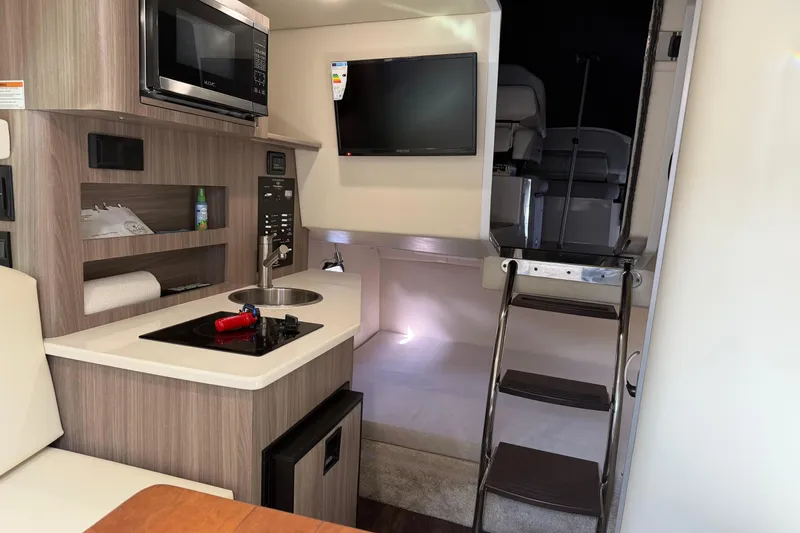 Slide: The Image of 2021 Regal 26 XO boat interior with kitchenette, TV, and ladder to cabin. - 24