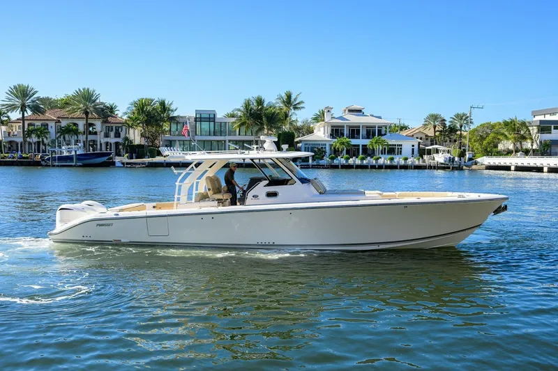 The Image of 2018 Pursuit S 408 Sport boat cruising on a sunny waterfront with luxury homes. - 1