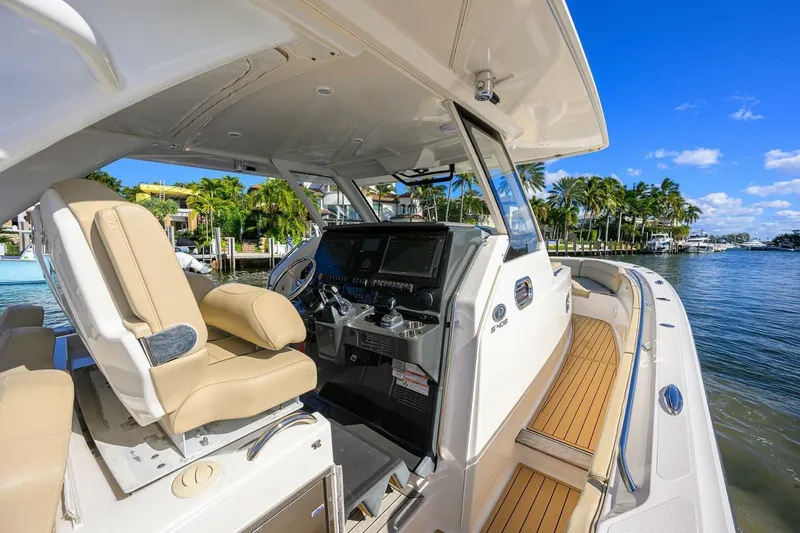 Slide: The Image of 2018 Pursuit S 408 Sport boat interior with helm, beige seating, and waterfront view. - 10