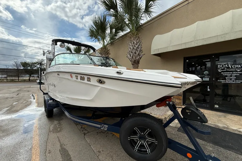 Slide: The Image of 2022 MasterCraft XT24 boat on trailer outside dealership, under cloudy sky. - 1