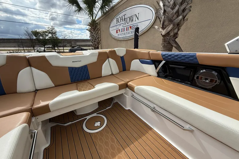 Slide: The Image of 2022 MasterCraft XT24 boat interior with tan and white seating, wood flooring, and speaker system. - 16