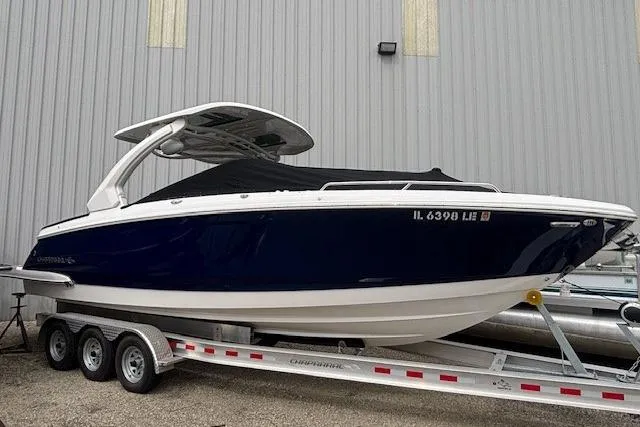 The Image of 2023 Chaparral 307 SSX boat on trailer, blue hull, covered, parked by a building. - 0