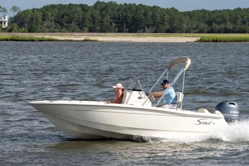 The Image of 2026 Scout 188 Sportfish boat cruising on a scenic lake with two passengers. - 1